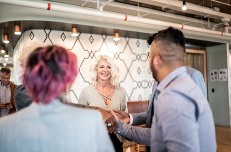 A group of people executing a handshake in an office while discussing event management.
