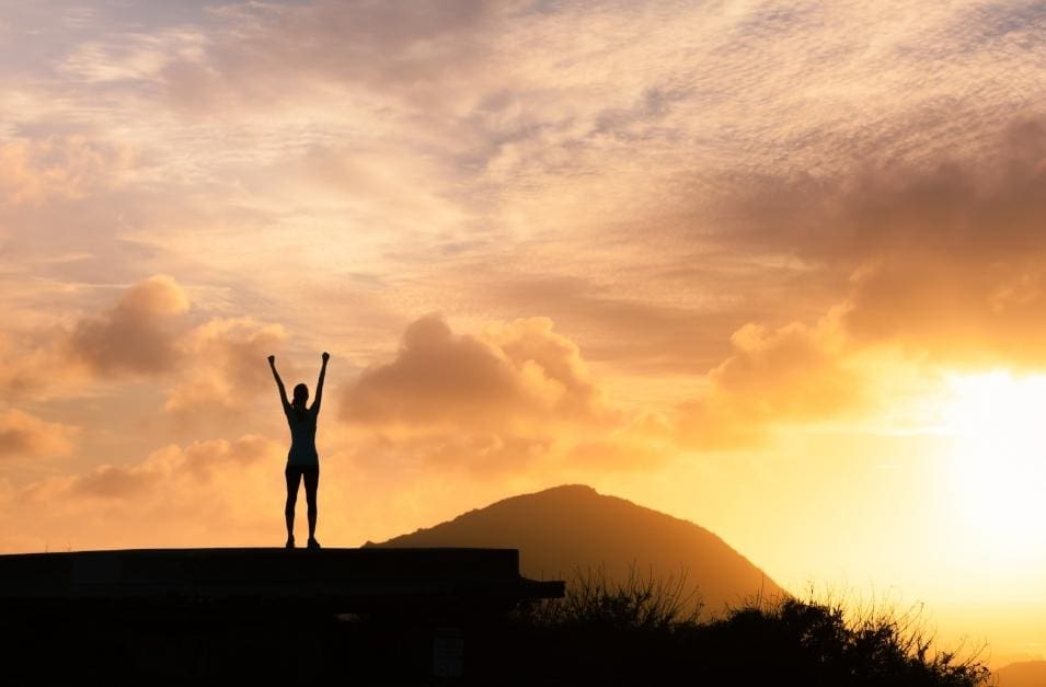 A person standing on top of a mountain at sunset, reviving their mojo.