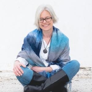Gayle Macdonald wearing glasses and a blue scarf sitting on the ground.