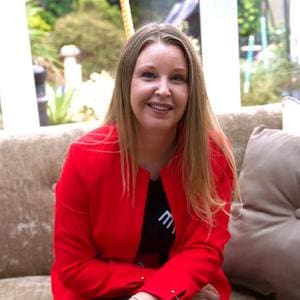 Lisa Ferris in a red jacket sitting on a couch.